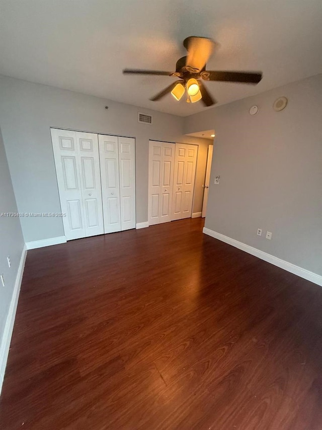 unfurnished bedroom featuring multiple closets, dark hardwood / wood-style floors, and ceiling fan