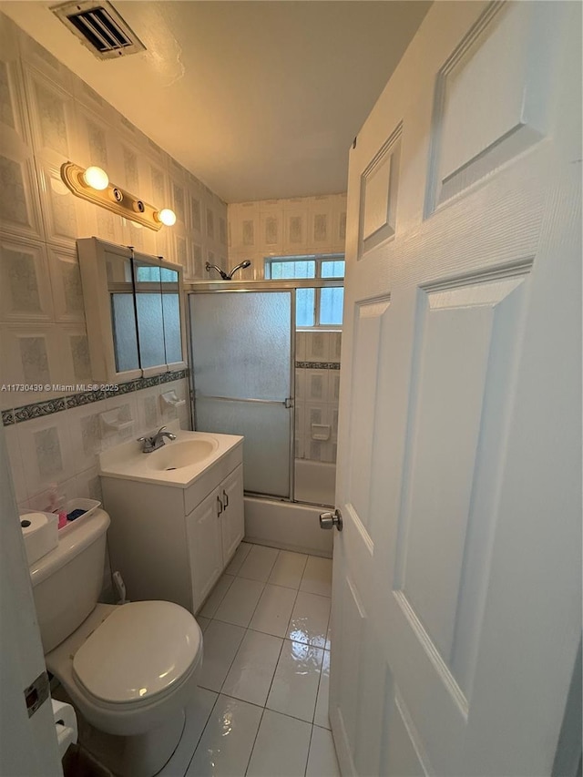 full bathroom with tile patterned flooring, tile walls, toilet, vanity, and bath / shower combo with glass door