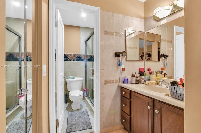 bathroom with vanity, toilet, tile walls, and a shower with door