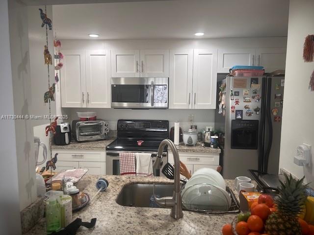 kitchen featuring light stone countertops, white cabinetry, appliances with stainless steel finishes, and sink