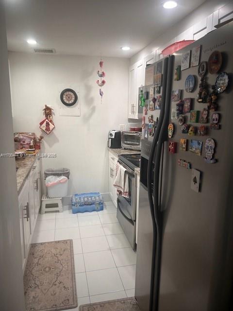 kitchen with stainless steel appliances, white cabinetry, light stone countertops, and light tile patterned floors