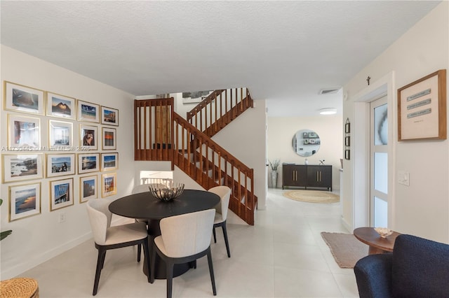 dining room featuring visible vents, light tile patterned flooring, a textured ceiling, baseboards, and stairs