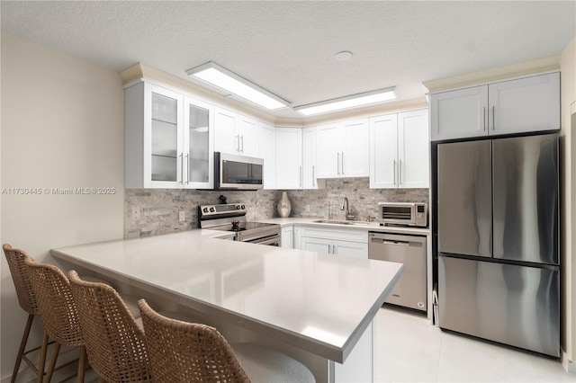 kitchen with a kitchen breakfast bar, appliances with stainless steel finishes, glass insert cabinets, and white cabinets