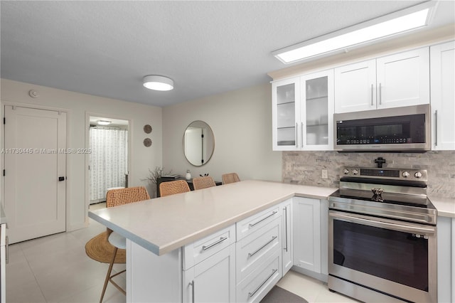 kitchen featuring stainless steel appliances, a breakfast bar, a peninsula, white cabinetry, and glass insert cabinets