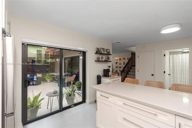 kitchen featuring light countertops, freestanding refrigerator, a breakfast bar, and white cabinetry