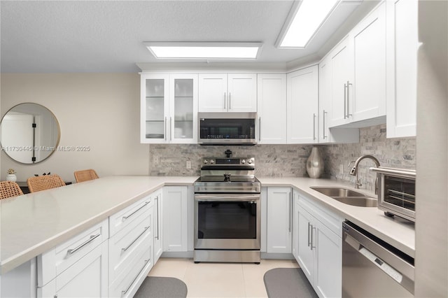 kitchen with appliances with stainless steel finishes, light countertops, glass insert cabinets, and a sink