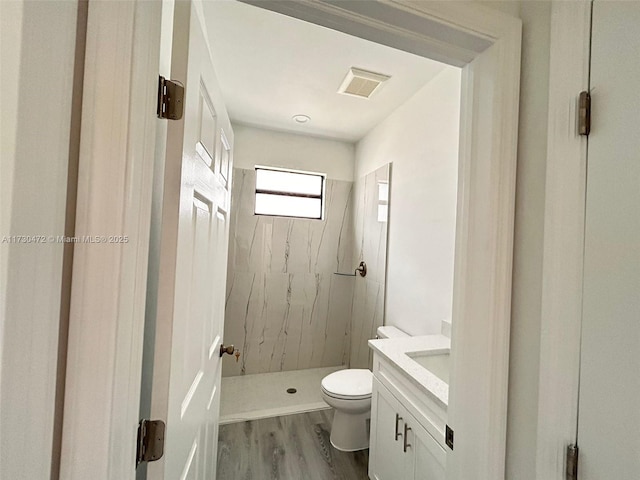 bathroom with hardwood / wood-style floors, toilet, vanity, and a tile shower