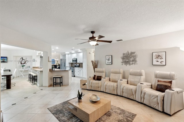 living room with ceiling fan, a textured ceiling, and light tile patterned flooring