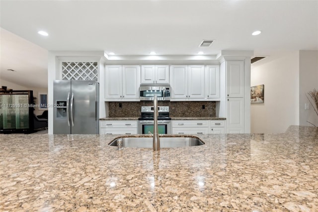 kitchen with backsplash, white cabinets, light stone countertops, and appliances with stainless steel finishes