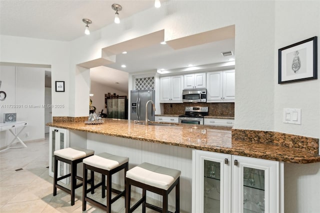 kitchen featuring white cabinets, dark stone countertops, kitchen peninsula, and appliances with stainless steel finishes