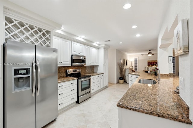 kitchen with white cabinets, stainless steel appliances, dark stone counters, sink, and kitchen peninsula