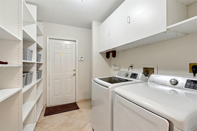 clothes washing area with cabinets, a textured ceiling, light tile patterned floors, and washing machine and dryer