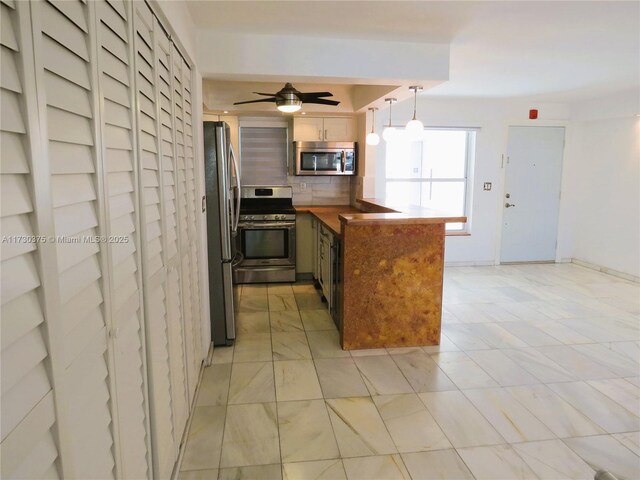 kitchen featuring pendant lighting, decorative backsplash, ceiling fan, kitchen peninsula, and stainless steel appliances