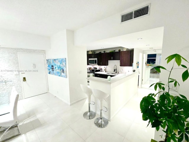 kitchen with appliances with stainless steel finishes, sink, a kitchen bar, dark brown cabinetry, and kitchen peninsula