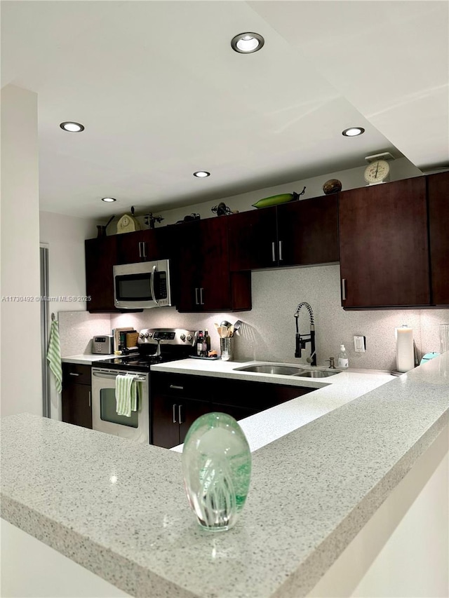 kitchen with dark brown cabinetry, sink, light stone counters, appliances with stainless steel finishes, and decorative backsplash