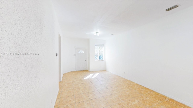 spare room featuring light tile patterned floors, visible vents, and baseboards