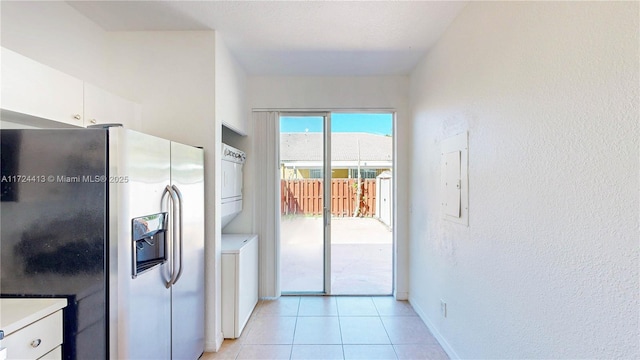 kitchen with light tile patterned flooring, light countertops, stacked washer and dryer, stainless steel refrigerator with ice dispenser, and white cabinetry