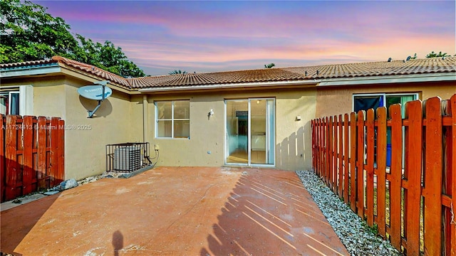 back of house at dusk with stucco siding, a patio, and fence