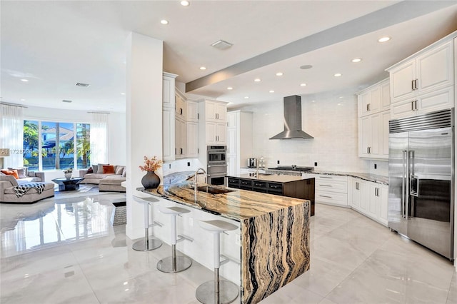 kitchen featuring wall chimney range hood, stainless steel appliances, white cabinetry, and kitchen peninsula