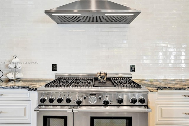 kitchen featuring double oven range, white cabinetry, dark stone countertops, and range hood