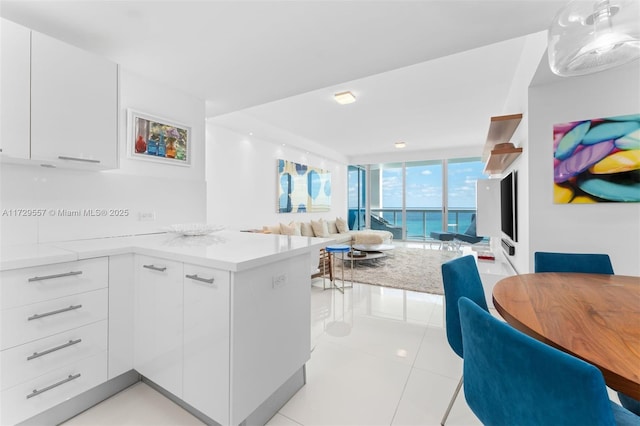 kitchen featuring hanging light fixtures, light tile patterned floors, kitchen peninsula, expansive windows, and white cabinets