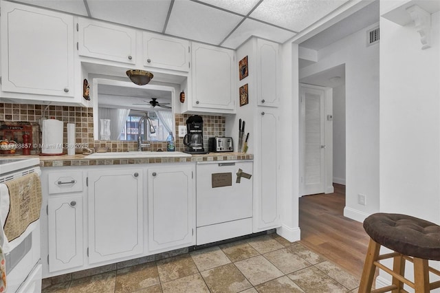 kitchen with white cabinets, dishwashing machine, a paneled ceiling, and sink