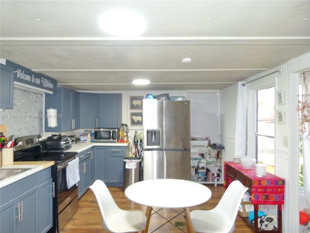 kitchen featuring appliances with stainless steel finishes, blue cabinets, and hardwood / wood-style floors