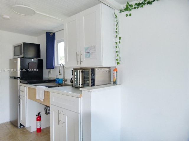 kitchen with white cabinetry, sink, stainless steel fridge, stove, and light tile patterned floors