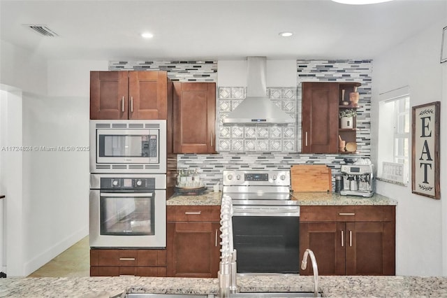 kitchen featuring backsplash, exhaust hood, appliances with stainless steel finishes, and light stone counters