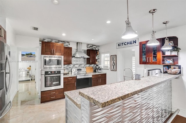 kitchen featuring hanging light fixtures, wall chimney exhaust hood, tasteful backsplash, a breakfast bar area, and stainless steel appliances