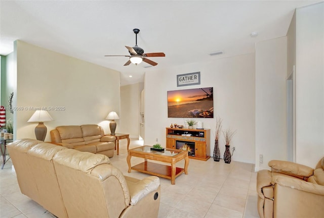 living room featuring a tile fireplace, light tile patterned floors, and ceiling fan