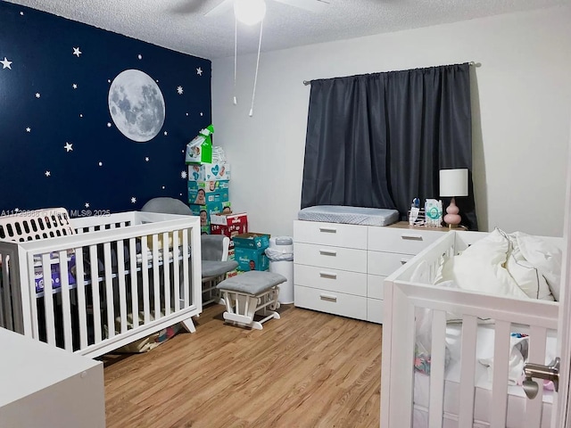 bedroom with ceiling fan, a textured ceiling, a nursery area, and light hardwood / wood-style flooring