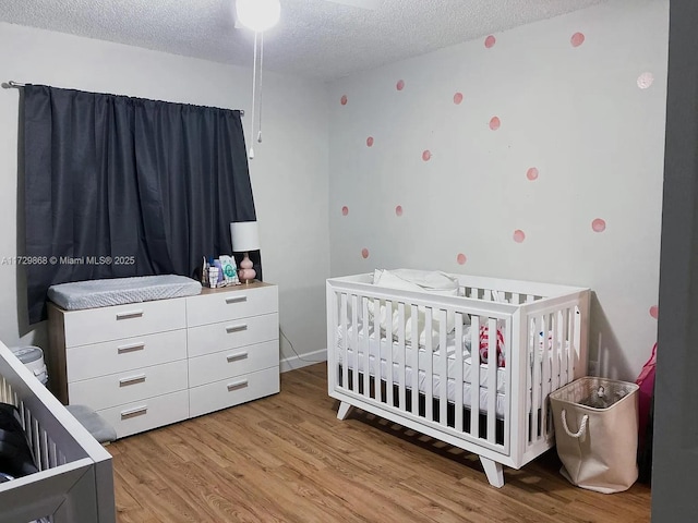 bedroom with a textured ceiling, a nursery area, and light hardwood / wood-style flooring