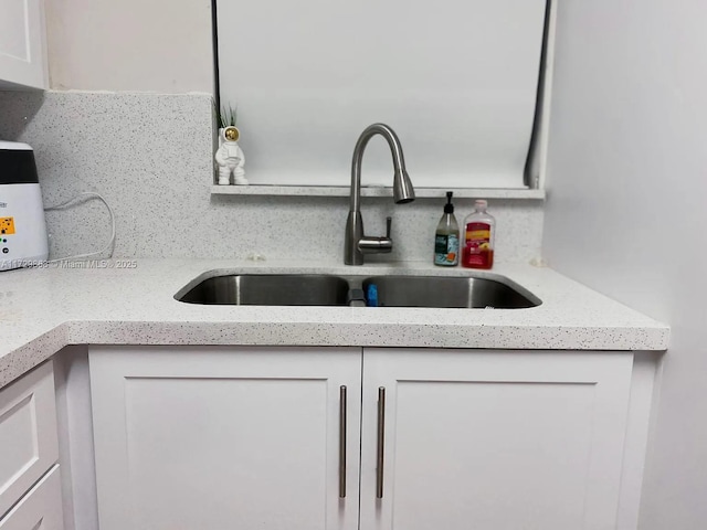 room details with sink, white cabinets, tasteful backsplash, and light stone counters