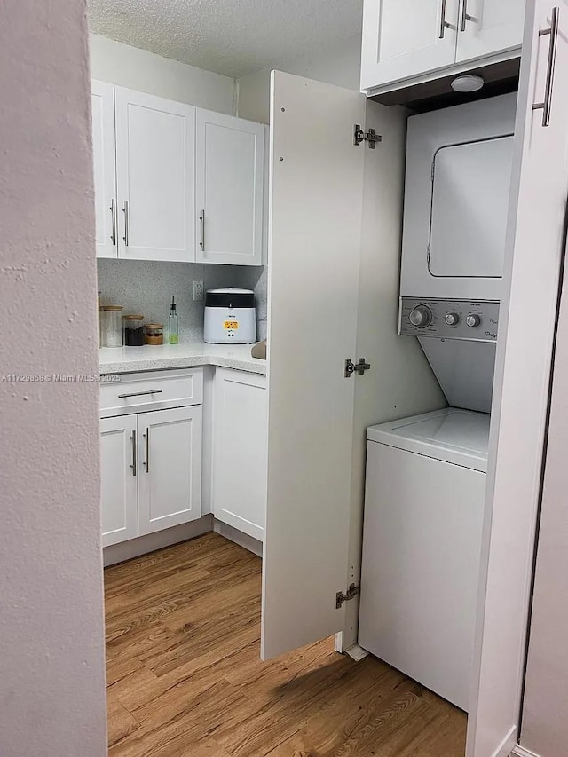 laundry room with a textured ceiling, cabinets, light hardwood / wood-style flooring, and stacked washer and clothes dryer