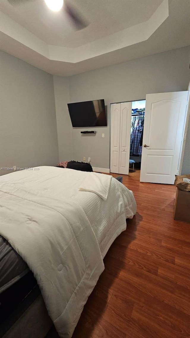 bedroom with ceiling fan, hardwood / wood-style flooring, a closet, and a tray ceiling