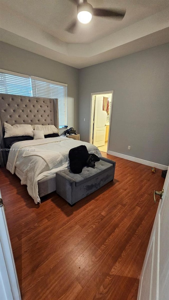 bedroom with ceiling fan, dark wood-type flooring, and a tray ceiling