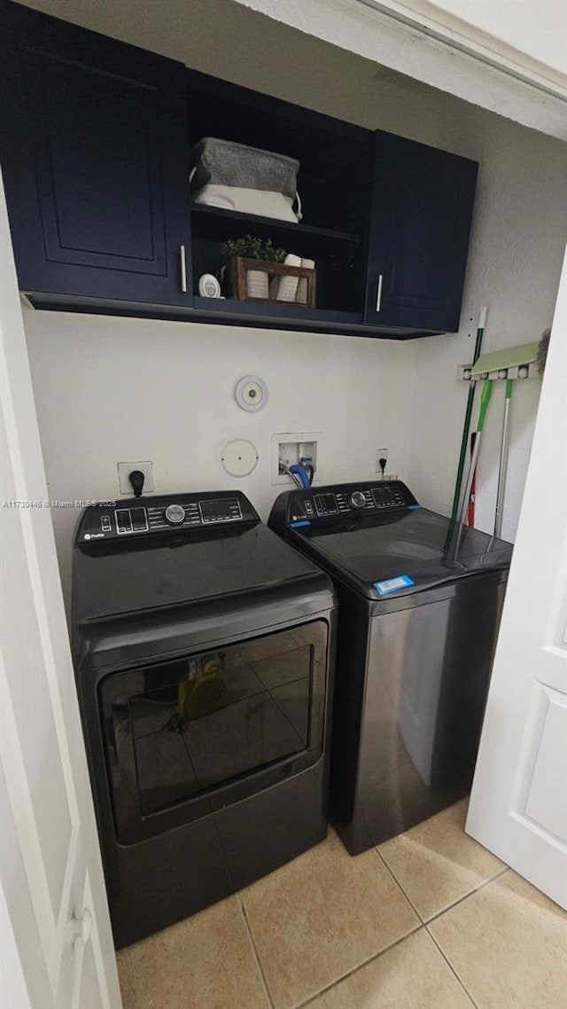 clothes washing area featuring cabinets, light tile patterned floors, and washing machine and clothes dryer