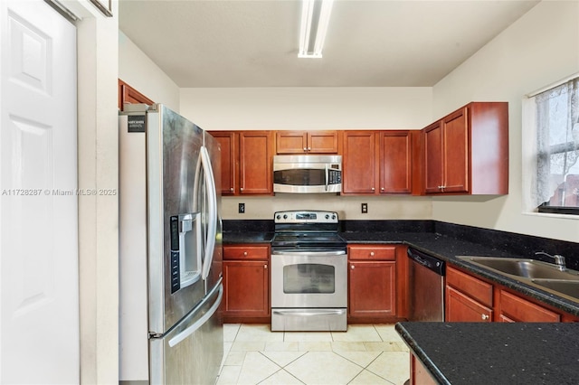 kitchen featuring sink, dark stone countertops, light tile patterned floors, and stainless steel appliances