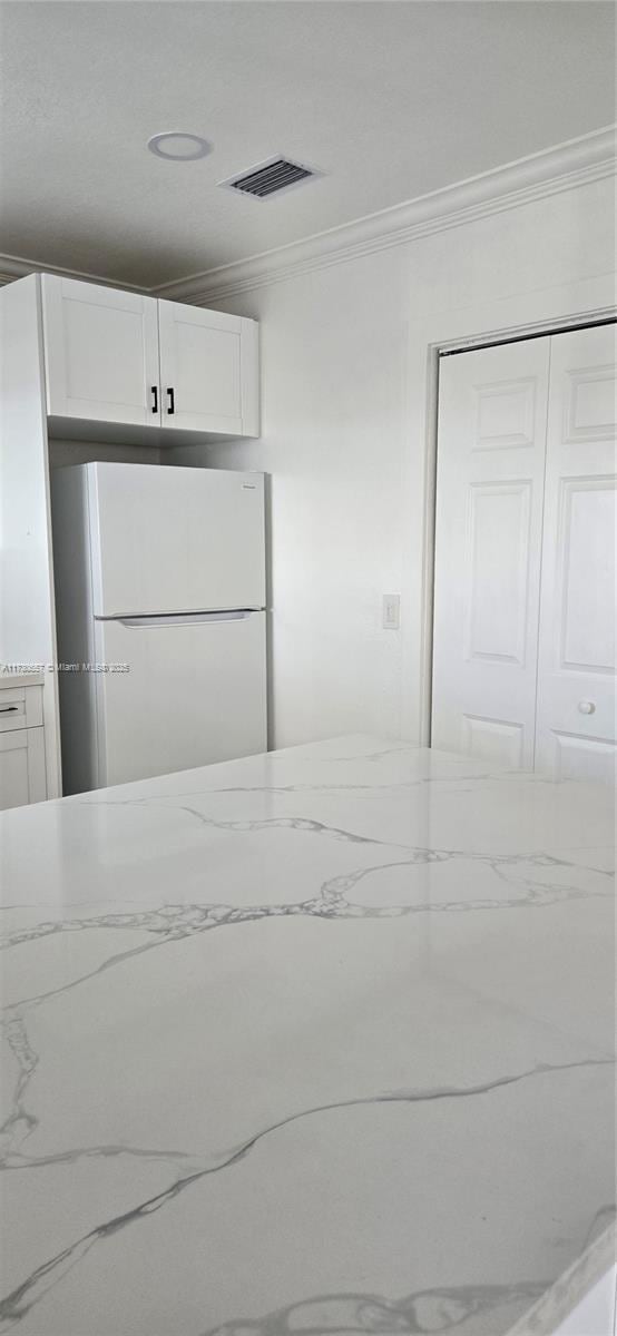 kitchen featuring crown molding, white refrigerator, and white cabinets