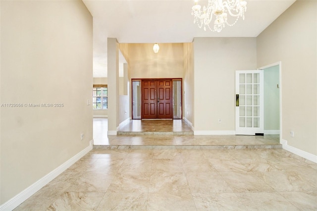 entrance foyer with baseboards, marble finish floor, an inviting chandelier, and a towering ceiling