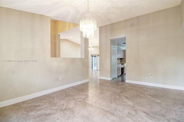 spare room with a chandelier, marble finish floor, and baseboards