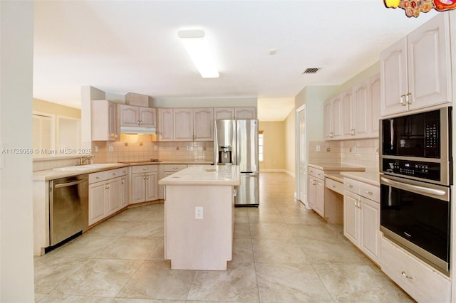kitchen with a center island, light countertops, under cabinet range hood, decorative backsplash, and stainless steel appliances