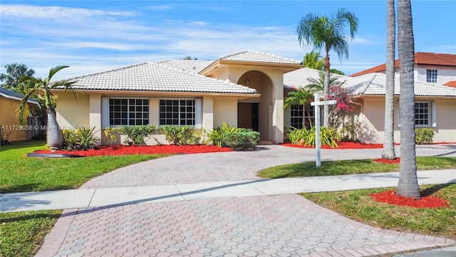mediterranean / spanish-style home with curved driveway, stucco siding, a tile roof, and a front yard