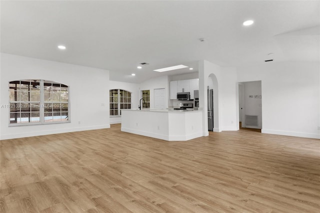 unfurnished living room featuring sink, light wood-type flooring, and vaulted ceiling