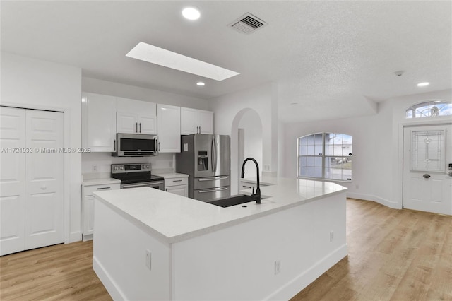 kitchen with stainless steel appliances, white cabinetry, light hardwood / wood-style floors, and an island with sink