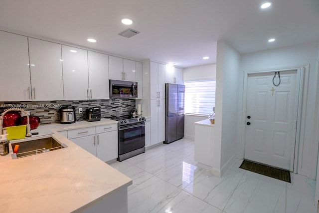 kitchen featuring sink, tasteful backsplash, white cabinetry, light stone countertops, and stainless steel appliances