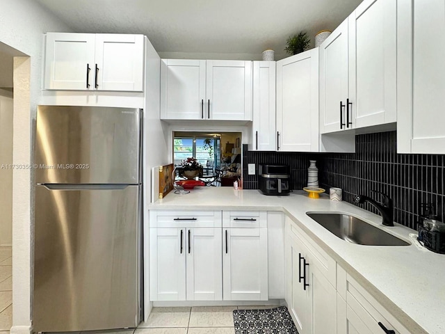 kitchen with white cabinetry, light tile patterned floors, decorative backsplash, sink, and stainless steel fridge