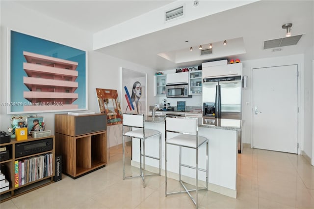 kitchen with light tile patterned floors, appliances with stainless steel finishes, white cabinetry, light stone counters, and a kitchen bar