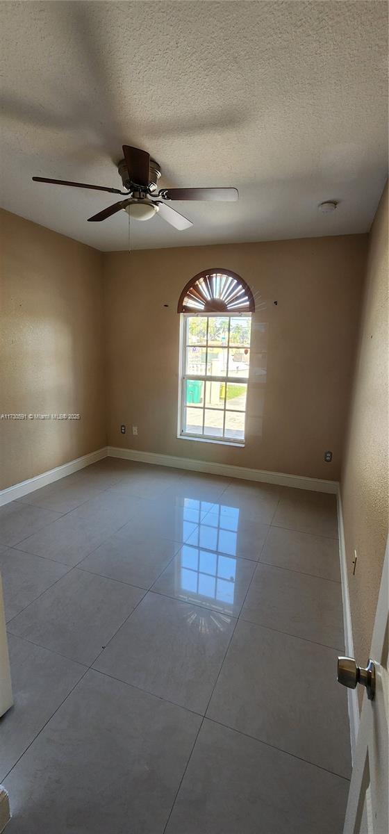 empty room with ceiling fan, light tile patterned floors, and a textured ceiling